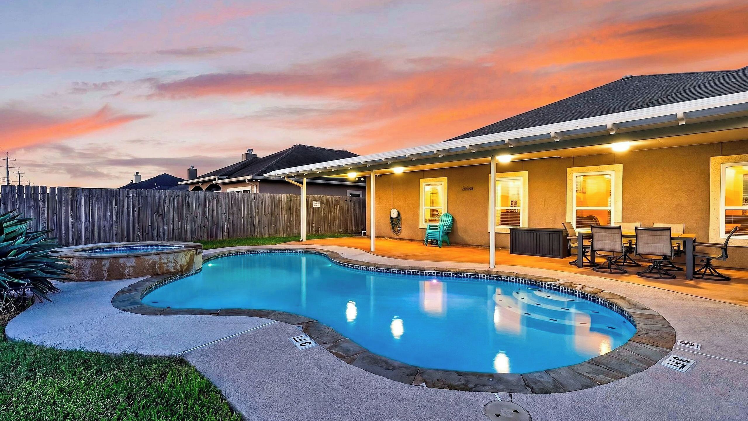 A backyard with a swimming pool, a covered patio area, and a wooden fence.