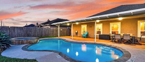 A backyard with a swimming pool, a covered patio area, and a wooden fence.