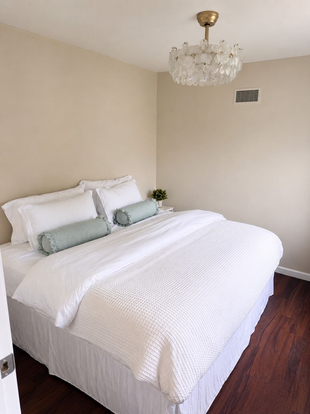 A bedroom with a large bed, a chandelier, and a small plant on the nightstand.