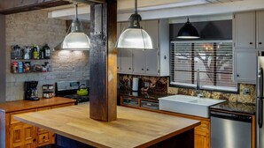 Een moderne keuken met een centraal eiland, hangende lampen en roestvrijstalen apparatuur.