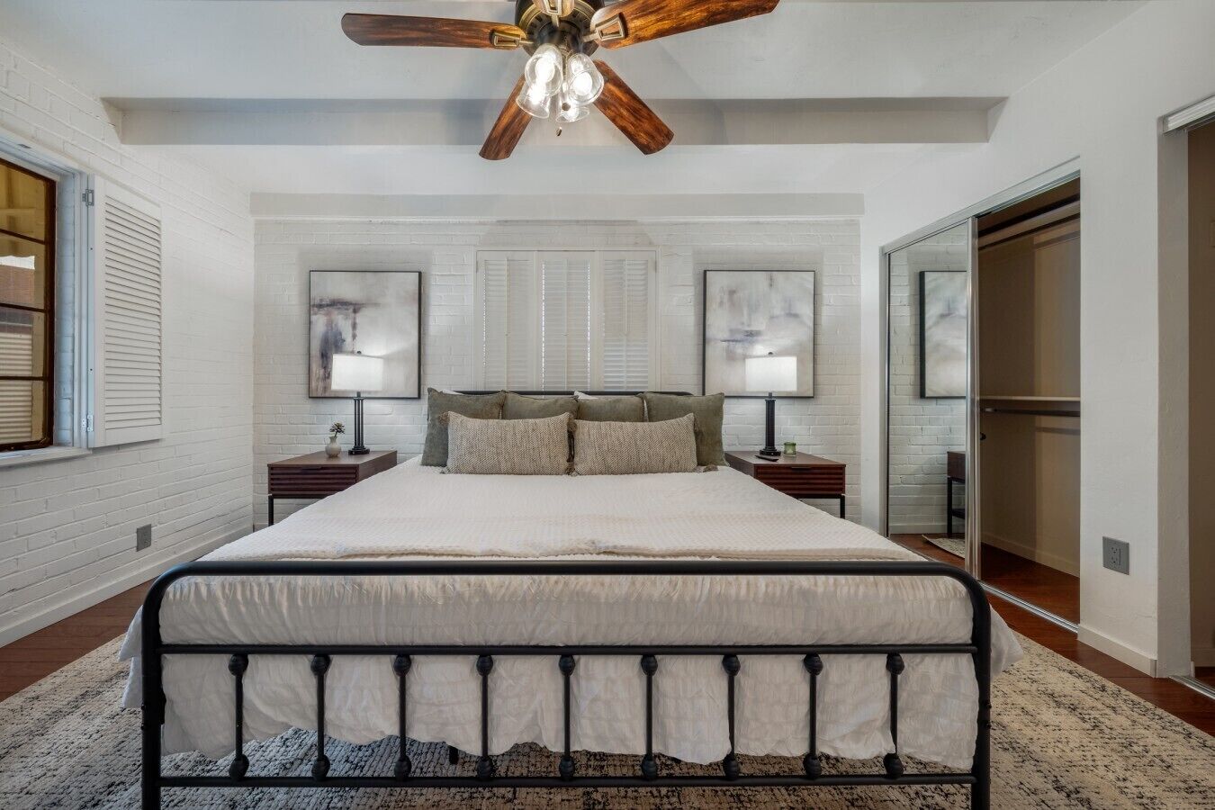 A bedroom with a large bed, two bedside tables, a ceiling fan, and a window with blinds.