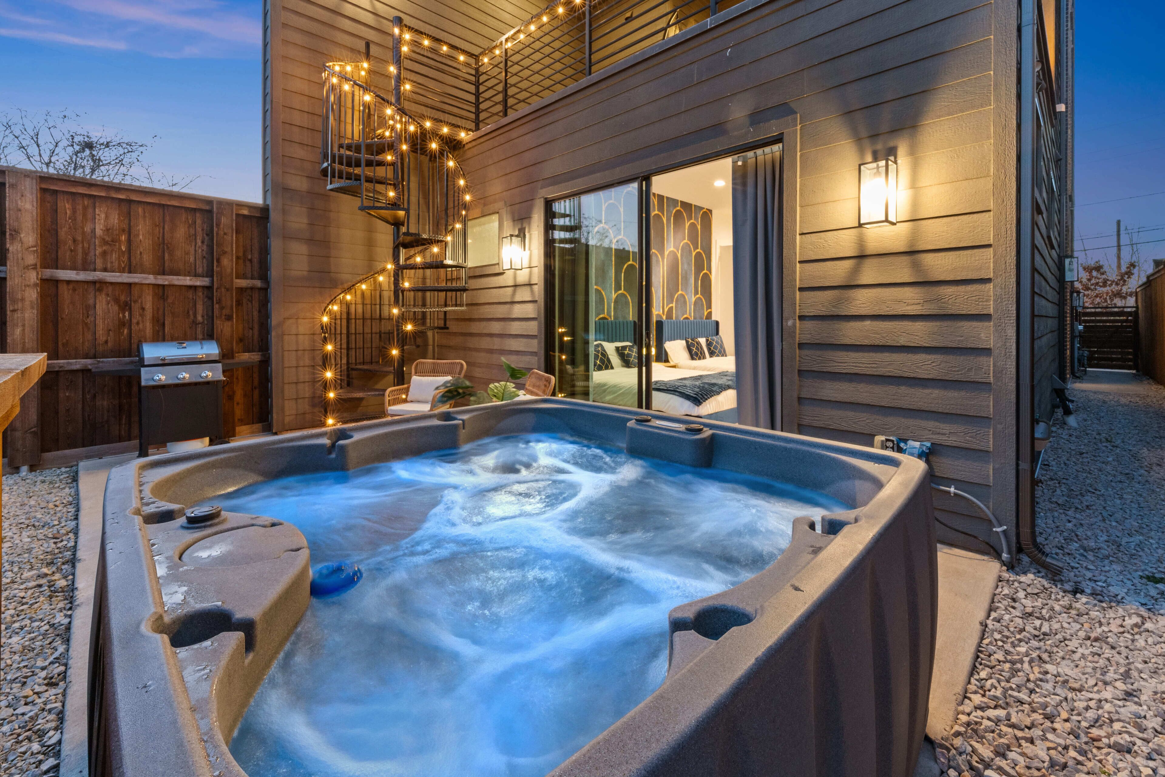 A hot tub in front of a wooden house with a balcony and string lights.