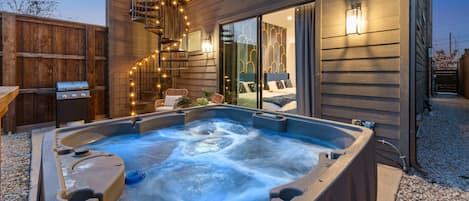 A hot tub in front of a wooden house with a balcony and string lights.