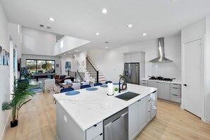 A modern kitchen with a central island, stainless steel appliances, and a dining area with a view. - Luxury 6BR Duplex Lofts with Hot Tub, Billiards, Balconies (Dallas)