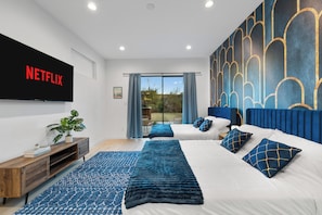 A modern bedroom with a large bed, a TV mounted on the wall, and a view of the outdoors. - Luxury 6BR Duplex Lofts with Hot Tub, Billiards, Balconies (Dallas)