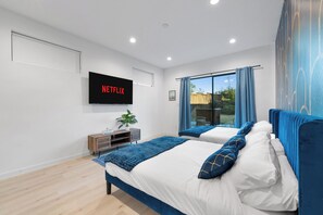 Ein modernes Schlafzimmer mit zwei Betten, einem an der Wand befestigten Fernseher und Blick ins Freie durch ein Fenster.