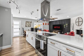 A modern kitchen with a large island, built-in oven, and a TV mounted on the wall. - Poolside Escape - Game Room - King Beds - Arcades (The Colony)