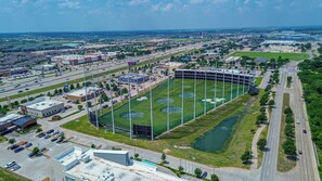 An aerial view of a stadium with multiple parking lots, a large field, and surrounding buildings. - Poolside Escape - Game Room - King Beds - Arcades (The Colony)