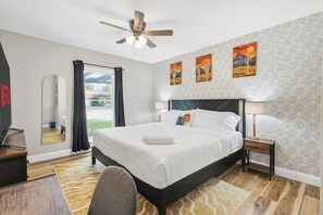 A hotel room with a bed, a desk, a chair, a ceiling fan, and a view of the outdoors. - Poolside Escape - Game Room - King Beds - Arcades (The Colony)