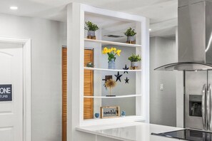 A kitchen with a white countertop, a stainless steel refrigerator, and a white shelving unit with decorative items. - Poolside Escape - Game Room - King Beds - Arcades (The Colony)