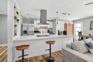 A modern kitchen with white cabinetry, stainless steel appliances, and a central island with bar stools. - Poolside Escape - Game Room - King Beds - Arcades (The Colony)