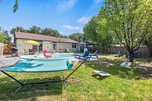 A backyard with a swimming pool, a hammock, and a covered patio area. - Poolside Escape | Game Area | King Beds | Arcades (The Colony)
