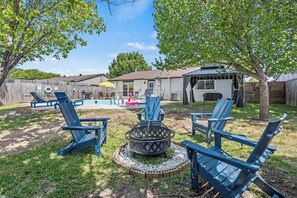 A backyard with a fire pit, outdoor seating, and a house in the background. - Poolside Escape | Game Area | King Beds | Arcades (The Colony)