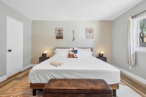 A bedroom with a large bed, two bedside tables with lamps, a window with curtains, and a zebra-patterned rug. - Poolside Escape - Game Room - King Beds - Arcades (The Colony)