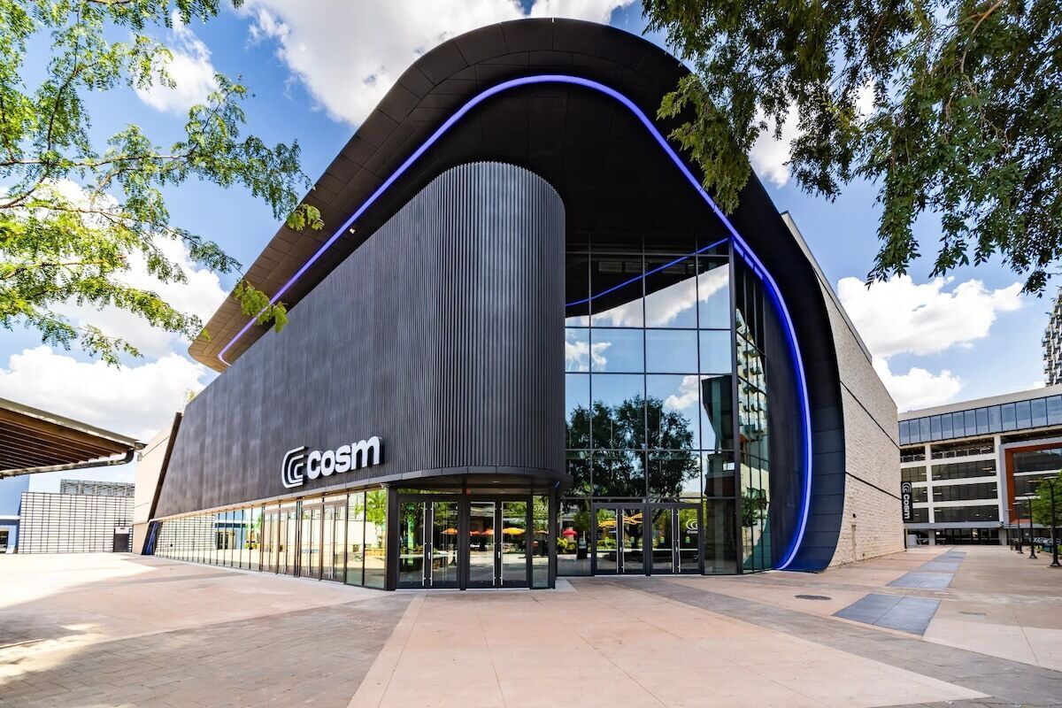 En moderne bygning med en buet facade, store glasruder og logoet 'COSIM' på siden.
