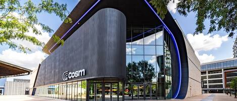 En moderne bygning med en buet facade, store glasruder og logoet 'COSIM' på siden.