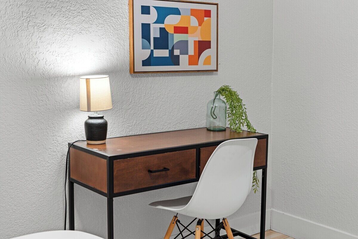 Uma mesa com uma lâmpada, uma cadeira e um quadro abstrato na parede.
