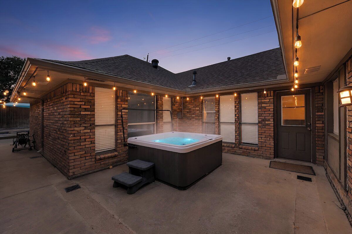 A hot tub in a backyard with a brick wall, steps, and string lights.