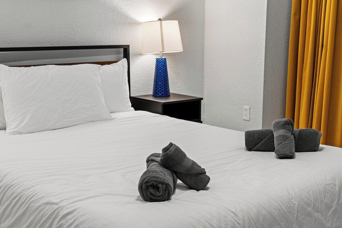 A neatly made bed with white linens, a blue lamp on a bedside table, and a set of towels.
