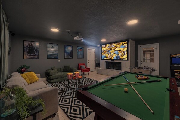 A living room with a pool table, a sofa, a red chair, and a projector screen. - Home Theater - Game Room - Pool - Hot Tub - Golf (Plano)