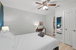 A hotel room with a bed, a desk, a chair, a ceiling fan, and a door. - Home Theater - Game Room - Pool - Hot Tub - Golf (Plano)