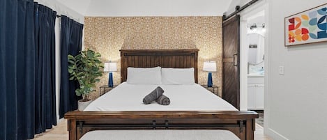 Une chambre à coucher avec un lit en bois, un banc, une plante en pot et un mur orné d’un motif géométrique.