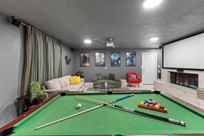 A room with a pool table, a projector screen, and a seating area with a couch and chairs. - Home Theater - Game Room - Pool - Hot Tub - Golf (Plano)