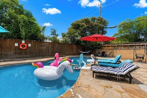 A backyard with a swimming pool, inflatable unicorn and swan floats, a red umbrella, and lounge chairs. - Home Theater - Game Room - Pool - Hot Tub - Golf (Plano)