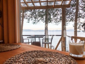 Una mesa de madera con individuales tejidos y un vaso de leche, con vista a un cuerpo de agua, árboles y una vista distante.