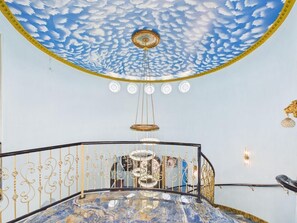 A room with a circular ceiling design, a chandelier, and a marble floor.