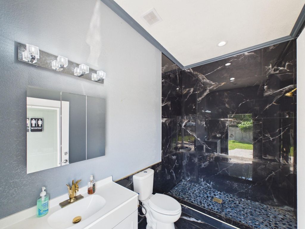 A modern bathroom with a marble shower wall, a white sink with a gold faucet, and a mirror above the sink.