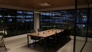 Un salón de conferencias con una larga mesa, sillas y paredes de vidrio que ofrecen vistas a la ciudad.