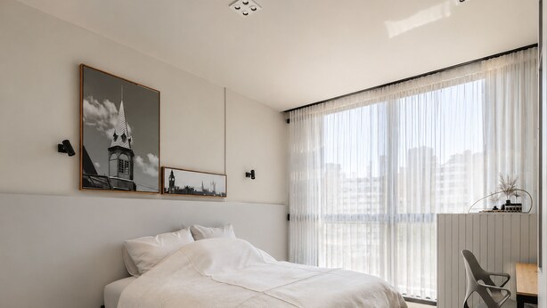 Un dormitorio moderno con una cama, un escritorio y una silla. Hay dos cuadros en la pared.