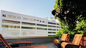 Una terraza en la azotea con sillones de mimbre, una planta en maceta y un edificio con señalización.