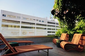 Una terraza en la azotea con sillones de mimbre, una planta en maceta y un edificio con señalización.