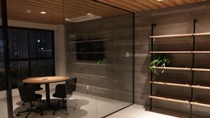 Un interior moderno con un separador de vidrio, una mesa redonda con sillas y una estantería con plantas.