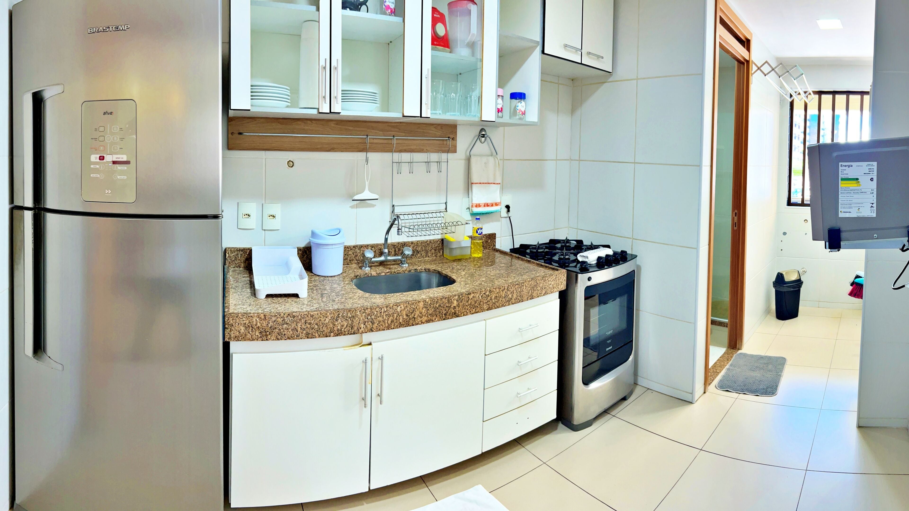 Una cocina moderna con refrigerador de acero inoxidable, horno empotrado, encimera de granito y armarios blancos.