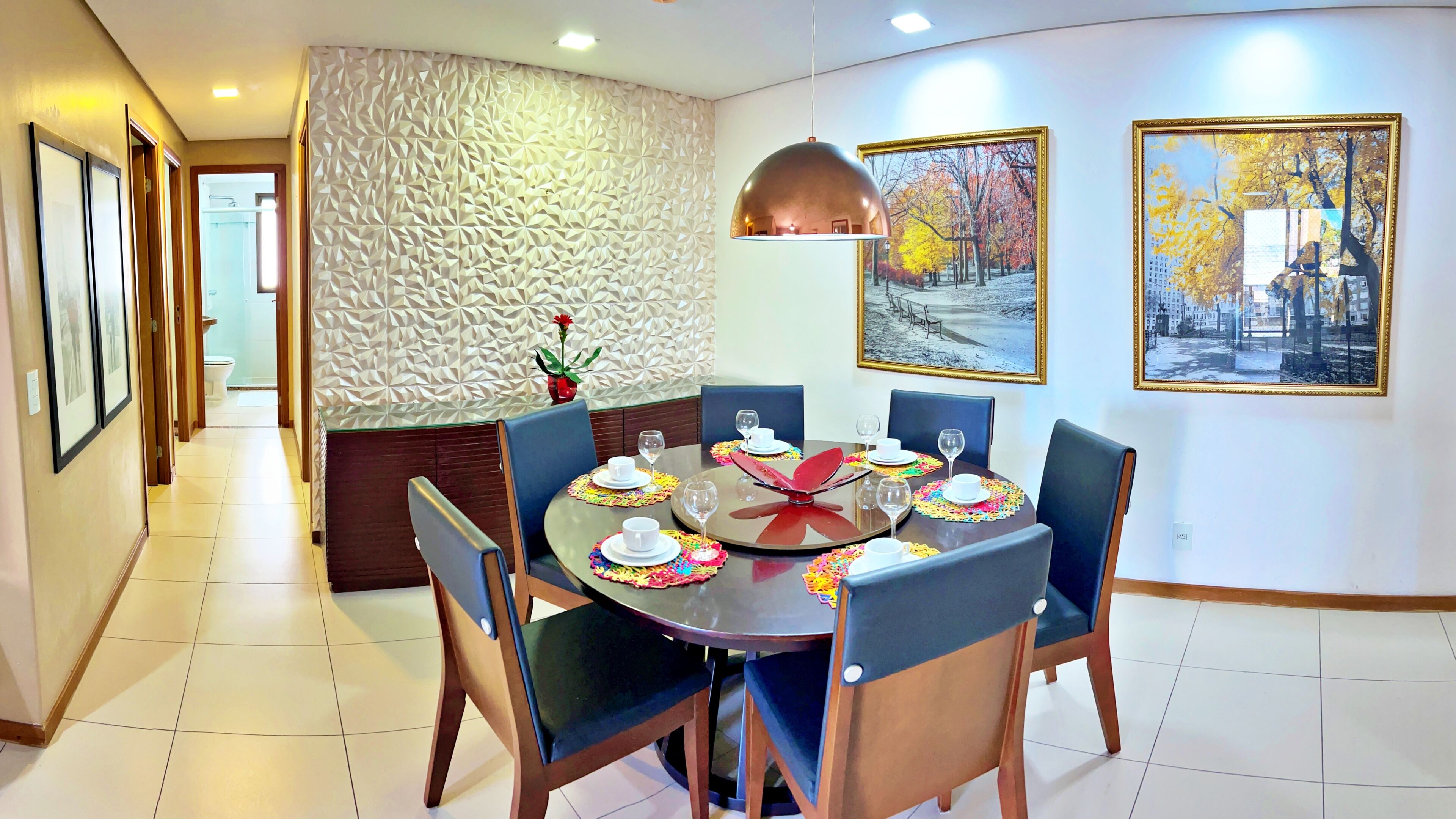 Un comedor con una mesa redonda dispuesta para seis personas, rodeada de sillas, una pared con textura y cuadros en la pared.