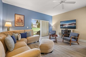 Ein Wohnzimmer mit einem beigen Sofa, einem Holztisch, einem blauen Sessel und einem an der Wand montierten Flachbildfernseher.