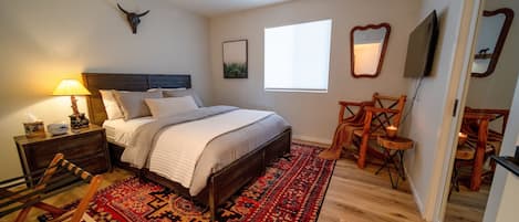 A bedroom with a bed, nightstands, a lamp, a mirror, a television, and a red patterned rug.