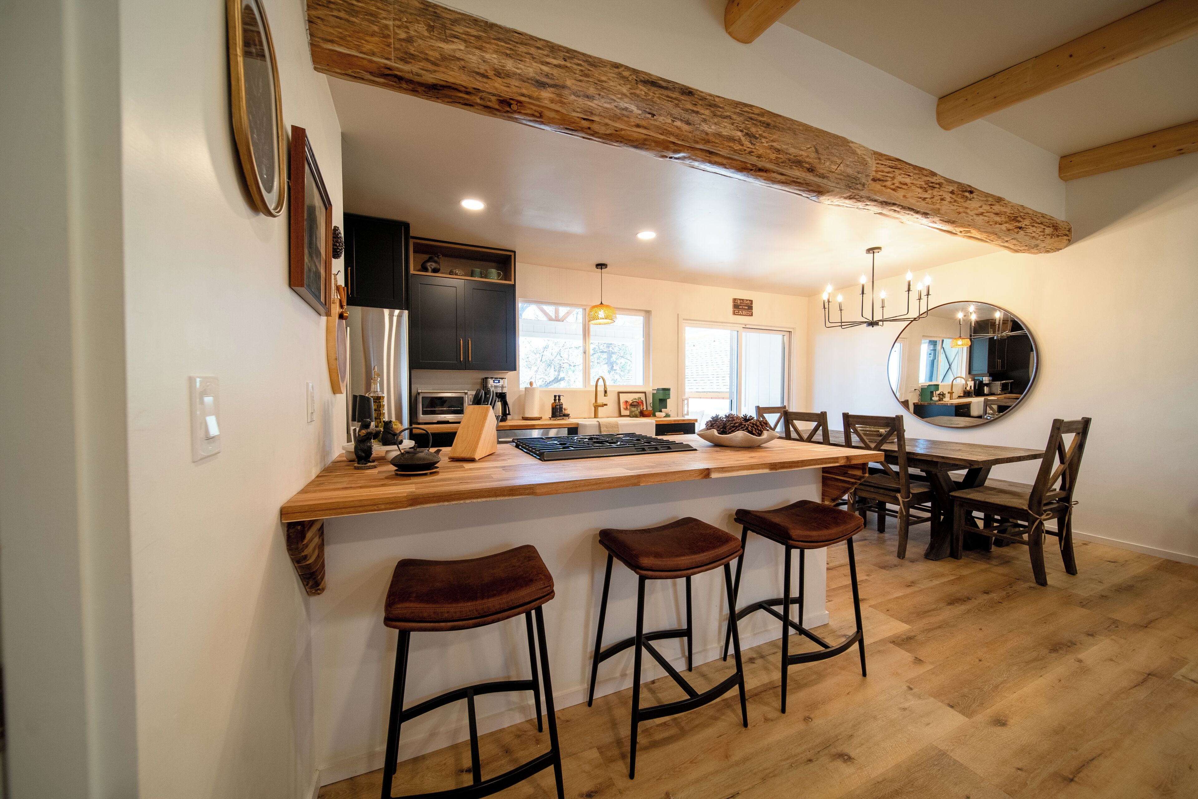 Una cocina moderna con vigas de madera, una isla grande con taburetes de bar y un comedor con un espejo redondo.