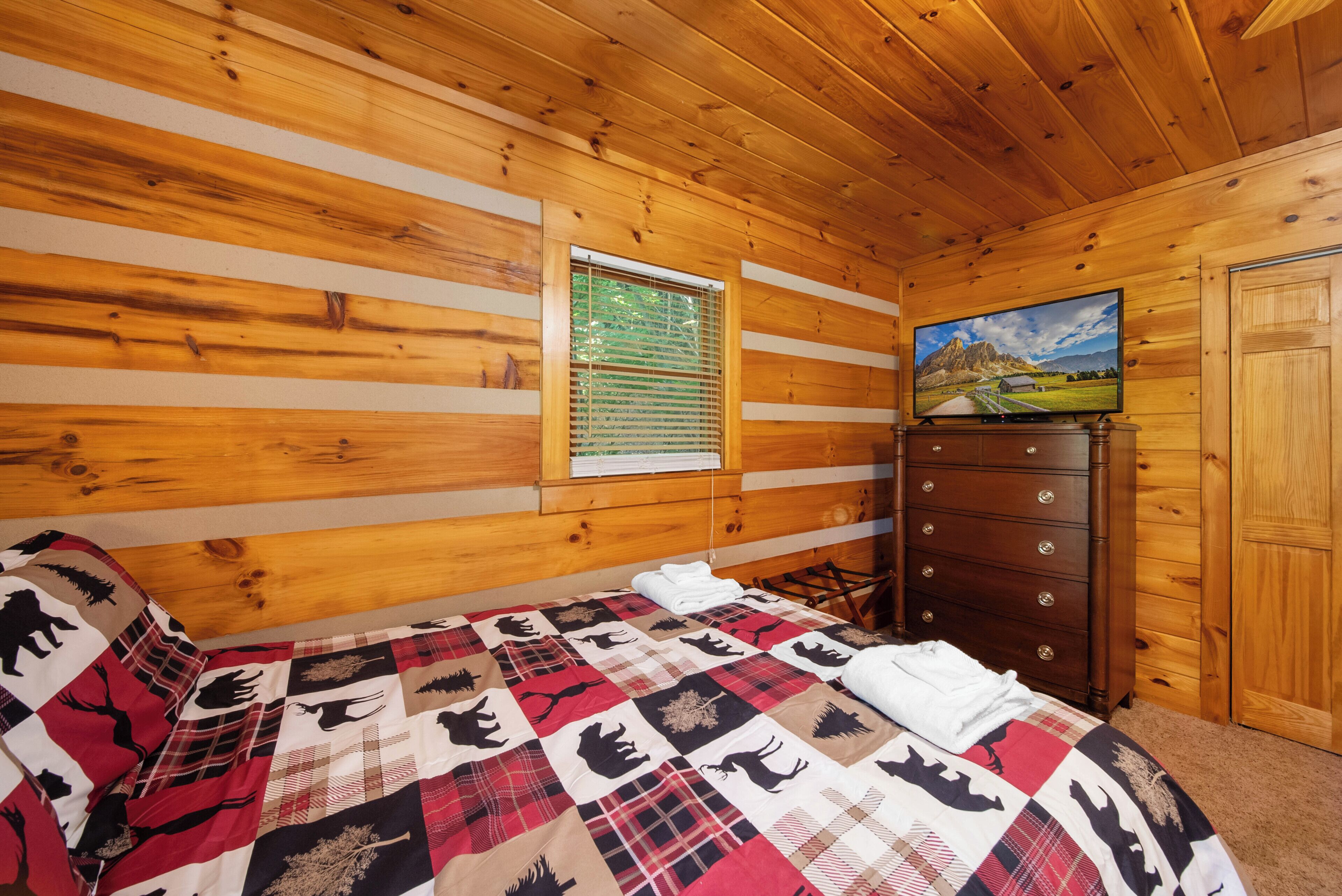 Una habitación de cabaña de madera con una cama, un aparador y un televisor en la pared.