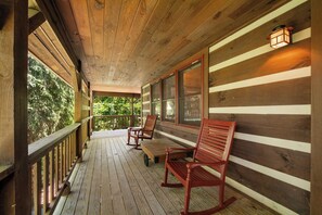 Une terrasse en bois avec une rambarde, deux fauteuils à bascule et un banc.
