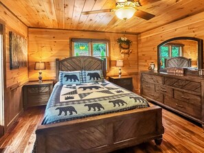 Ein Schlafzimmer einer Holzhütte mit einem Bett, Nachttischen, einer Kommode und einem Deckenventilator.