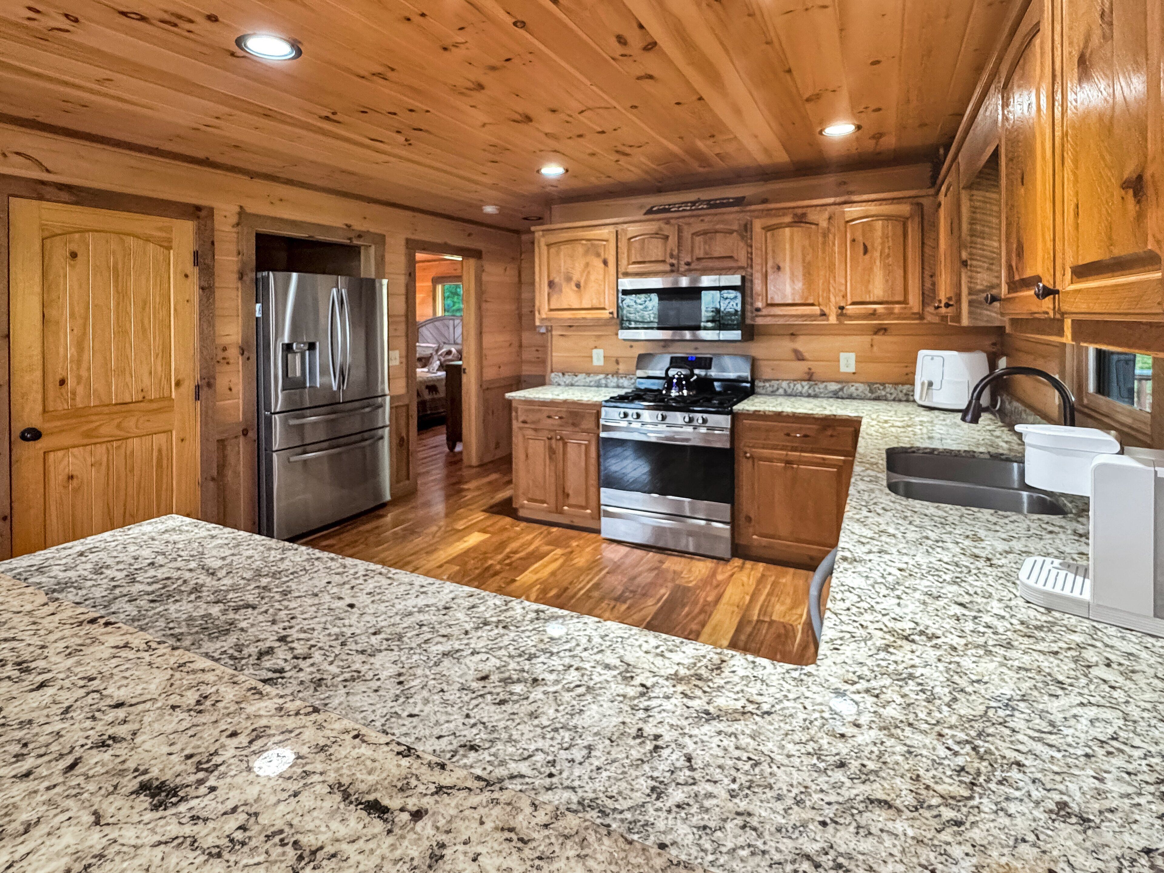 A kitchen with wooden cabinets, granite countertops, stainless steel appliances, and a view into the dining area.