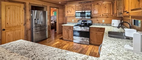 A kitchen with wooden cabinets, granite countertops, stainless steel appliances, and a view into the dining area.