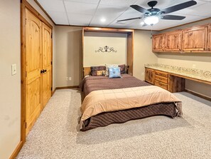 Ein Schlafzimmer mit Bett, Holzschrank, Deckenventilator und einer kleinen Schreibtischzeile.