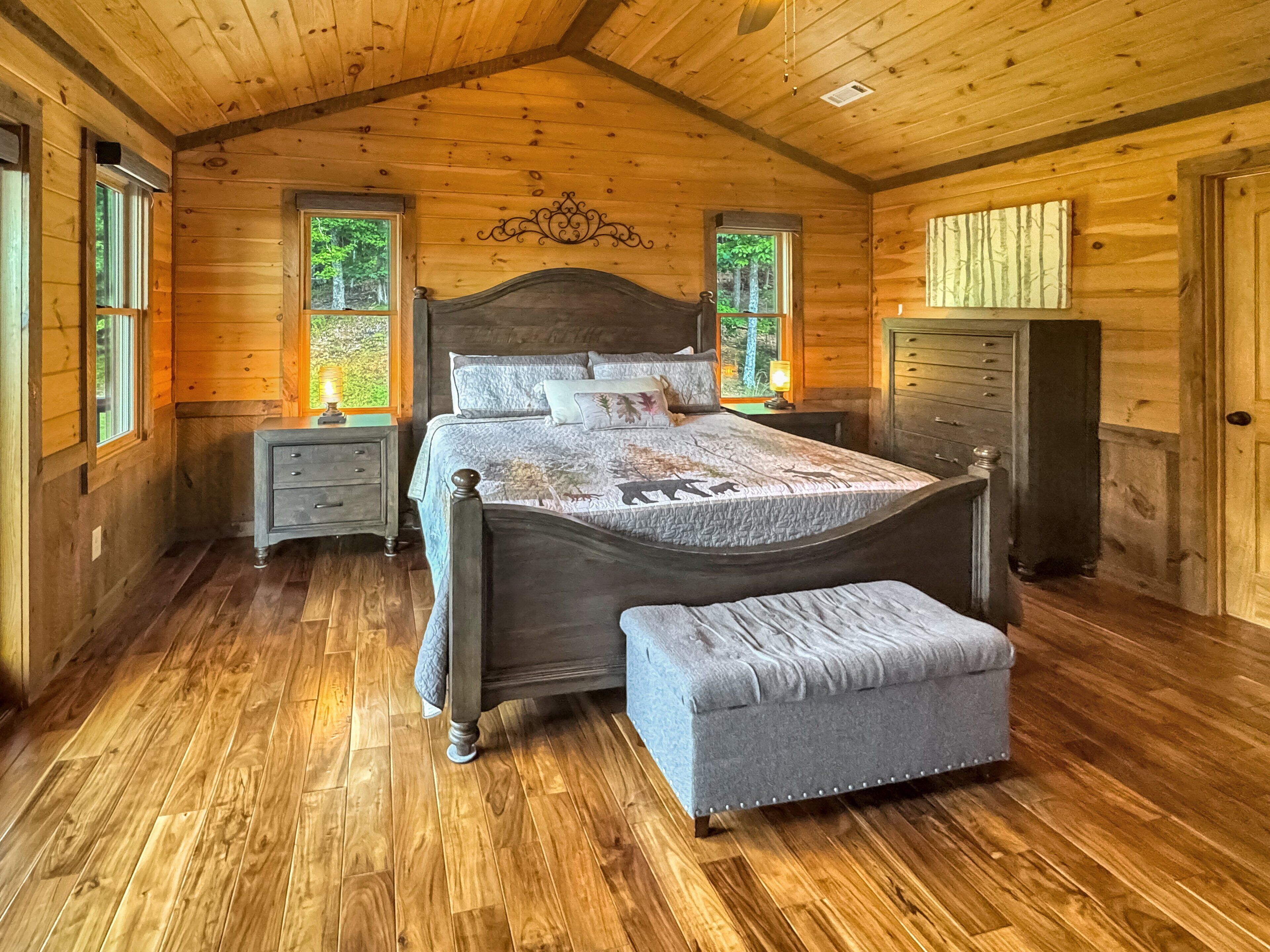 Quarto de cabana de madeira com cama, mesas de cabeceira, cômoda e um banco.