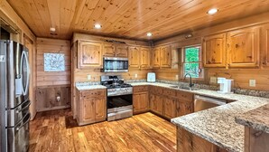 A kitchen with wooden cabinets, granite countertops, stainless steel appliances, and a herringbone-patterned floor.