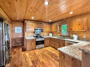 A kitchen with wooden cabinets, granite countertops, stainless steel appliances, and a herringbone-patterned floor.